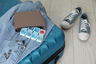 Suitcase with pill box and denim shirt on floor, closeup
