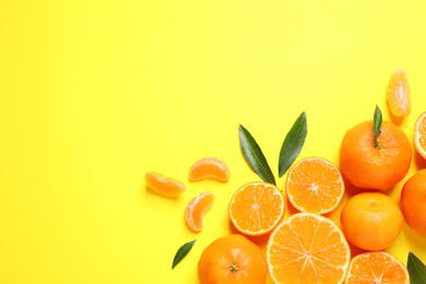 Flat lay composition with fresh ripe tangerines and leaves on yellow background, space for text. Citrus fruit