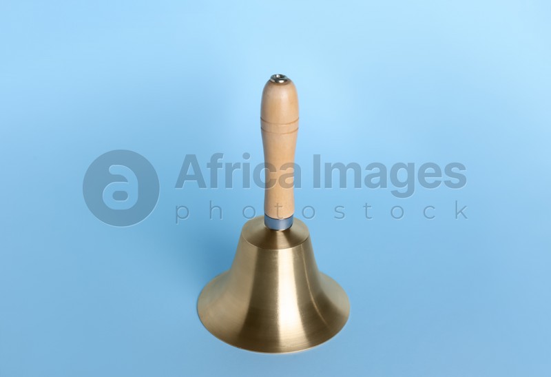 Golden school bell with wooden handle on light blue background