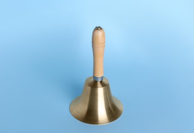 Golden school bell with wooden handle on light blue background
