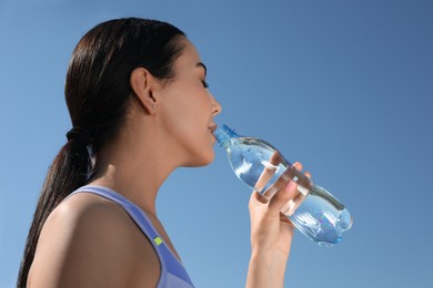 Beautiful young sportswoman drinking water outdoors. Refreshing drink