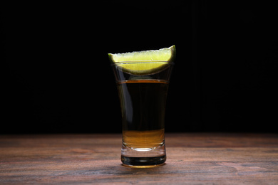 Mexican Tequila shot with lime slice on wooden table against black background
