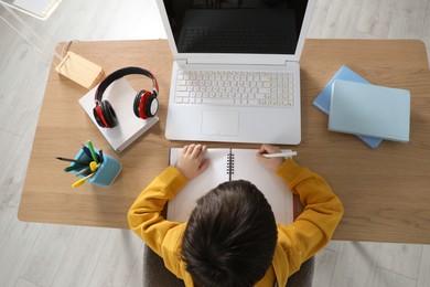 Photo of Cute little boy with modern laptop studying online at home, top view. E-learning