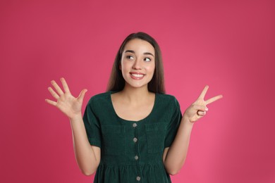 Woman showing number seven with her hands on pink background