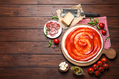 Flat lay composition with base and ingredients on wooden table, space for text. Pepperoni pizza recipe