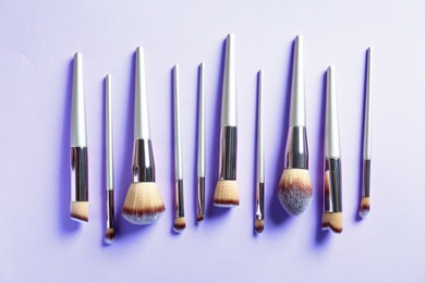 Many different makeup brushes on lilac background, flat lay