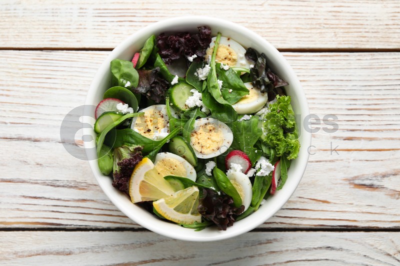 Photo of Delicious salad with boiled eggs, vegetables and lemon in bowl on white wooden table, top view