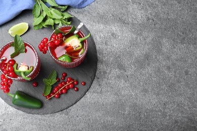 Photo of Glasses of spicy red currant cocktail with jalapeno and mint on grey table, flat lay. Space for text