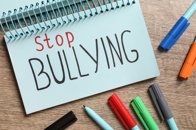 Text Stop Bullying written in notebook and markers on wooden table, flat lay