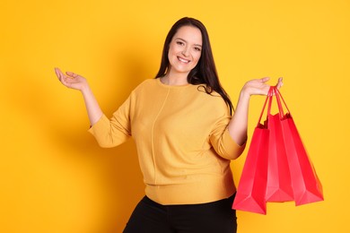 Beautiful overweight woman with shopping bags on yellow background