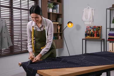 Dressmaker cutting fabric by following chalked sewing pattern in workshop