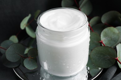 Jar of hand cream and eucalyptus branches on grey background, closeup