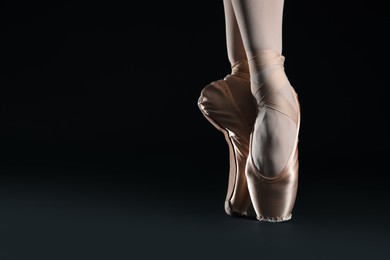 Photo of Ballerina in pointe shoes dancing on black background, closeup. Space for text