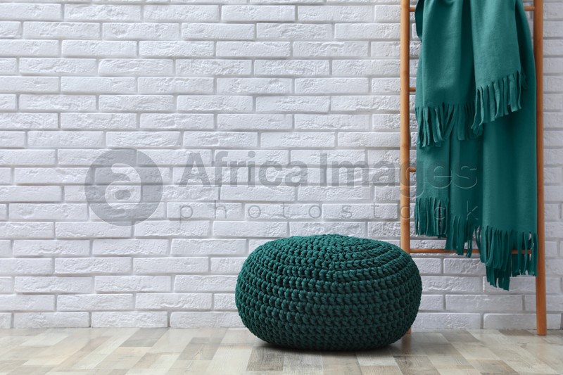 Photo of Stylish knitted pouf and ladder with plaid near white brick wall indoors, space for text. Interior design