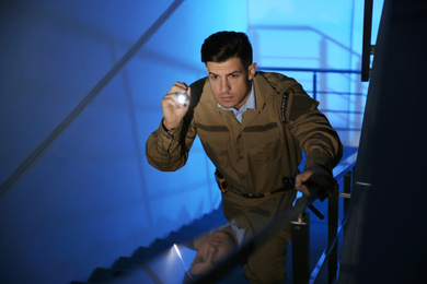 Photo of Professional security guard with flashlight on stairs in dark room
