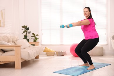 Overweight woman doing exercise with dumbbells at home, space for text