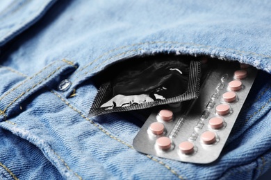 Black condom and birth control pills in pocket of jeans, closeup. Safe sex concept