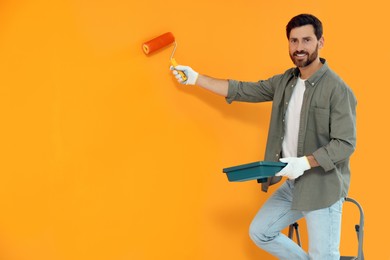Photo of Happy designer painting orange wall with roller, space for text