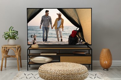 Modern TV set on wooden stand in room. Scene of romantic movie on screen
