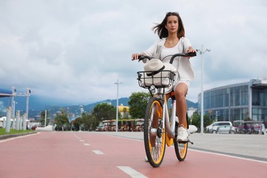 Beautiful young woman riding bicycle on lane in city. Space for text