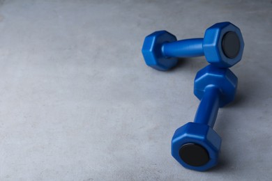 Photo of Blue vinyl dumbbells on light grey table. Space for text