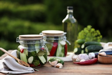 Jars of delicious pickled cucumbers and ingredients on wooden table against blurred background. Space for text
