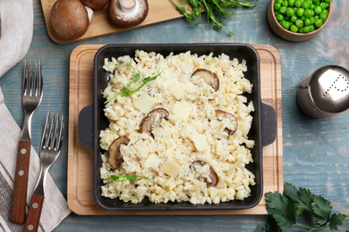 Photo of Delicious risotto with cheese and mushrooms on light blue wooden table, flat lay