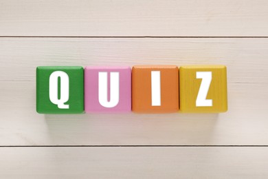 Colorful cubes with word Quiz on white wooden table, flat lay