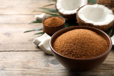 Natural coconut sugar in bowl on wooden table, space for text