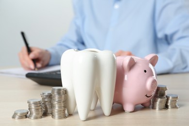 Ceramic model of tooth, piggy bank and coins on wooden table. Expensive treatment