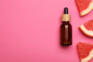 Bottle of citrus essential oil and fresh grapefruit slices on pink background, flat lay. Space for text