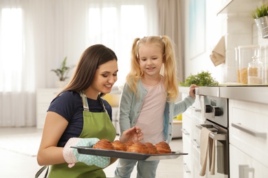 Daughter and mother with tray of oven baked buns in kitchen