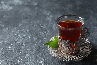 Photo of Glass of traditional Turkish tea in vintage holder on grey textured table, closeup. Space for text
