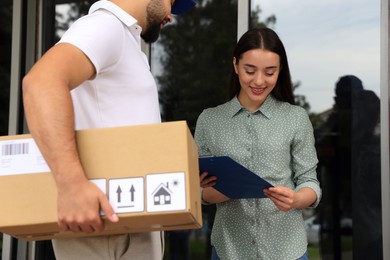Woman signing for delivered parcel near entrance outdoors