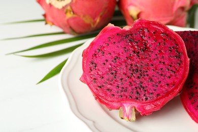 Plate of delicious cut red pitahaya fruit on white table, closeup