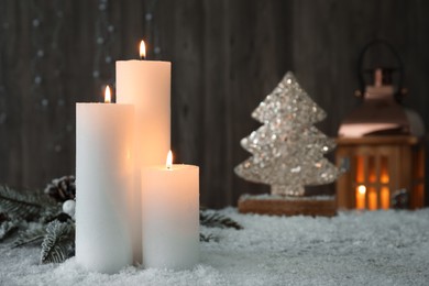 Photo of Burning candles and Christmas decor on artificial snow. Space for text