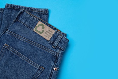 Jeans with recycling label on light blue background, top view. Space for text