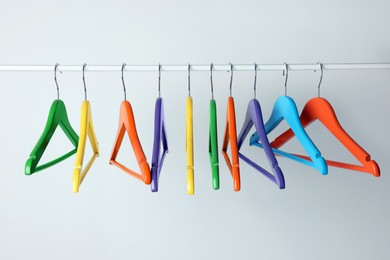 Bright clothes hangers on metal rail against light background