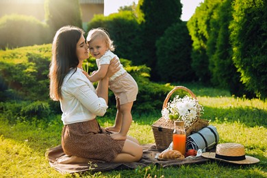 Mother and her baby daughter hugging while having picnic in garden on sunny day