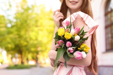 Teenage girl with bouquet of tulips on city street, closeup. Space for text