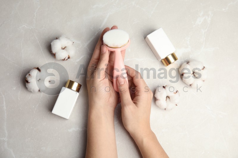 Photo of Woman with stylish face cleansing brush at light grey table, top view. Cosmetic accessory