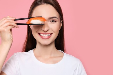 Photo of Funny young woman holding sushi with chopsticks on pink background