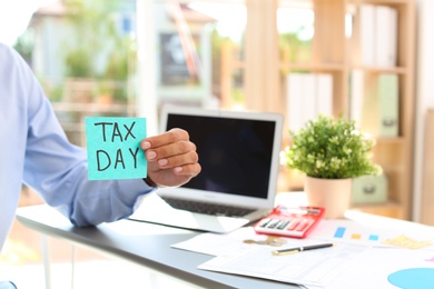 Man holding card with words TAX DAY indoors