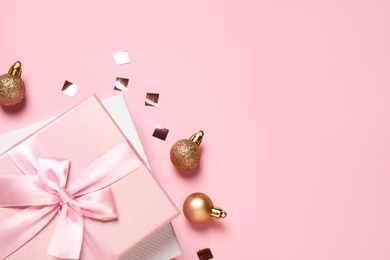 Beautiful gift boxes, golden Christmas balls and confetti on pink background, flat lay. Space for text
