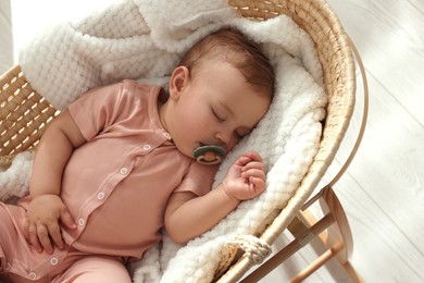 Cute little baby with pacifier sleeping in wicker crib at home, above view