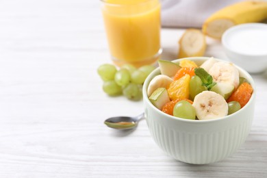 Delicious fresh fruit salad in bowl on white wooden table, space for text
