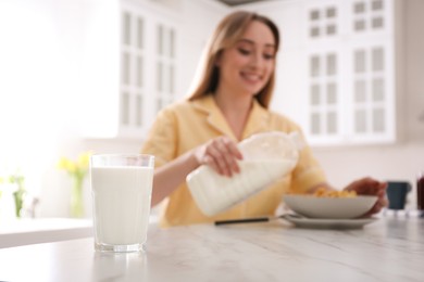Woman with gallon bottle and breakfast cereal at white marble table in kitchen, focus on glass of milk