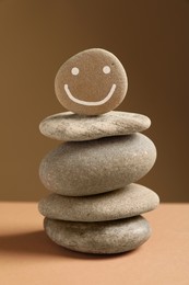 Stack of stones with drawn happy face on table against dark beige background. Zen concept