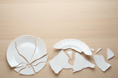 Two broken ceramic plates on wooden table, flat lay. Space for text