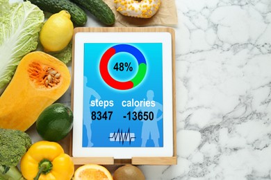 Photo of Tablet with weight loss calculator application and food products on white marble table, flat lay. Space for text